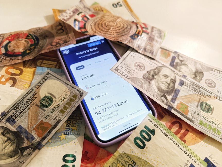 Exportação Brasileira. — A smartphone displaying a currency converter surrounded by dollar and euro banknotes, highlighting